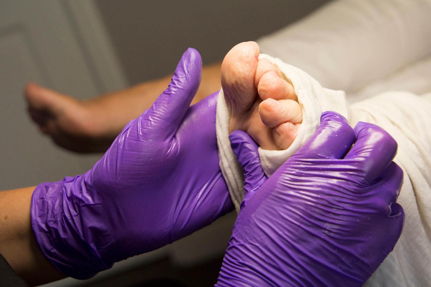 Margriet behandelt met handschoenen aan een voet tijdens een pedicurebehandeling